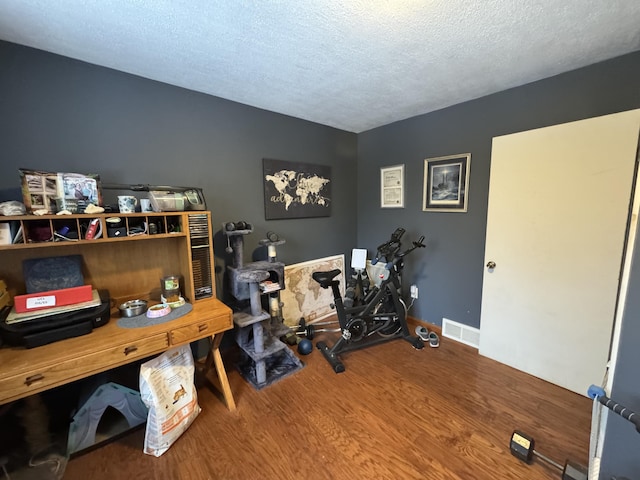 home office featuring a textured ceiling, wood finished floors, visible vents, and baseboards