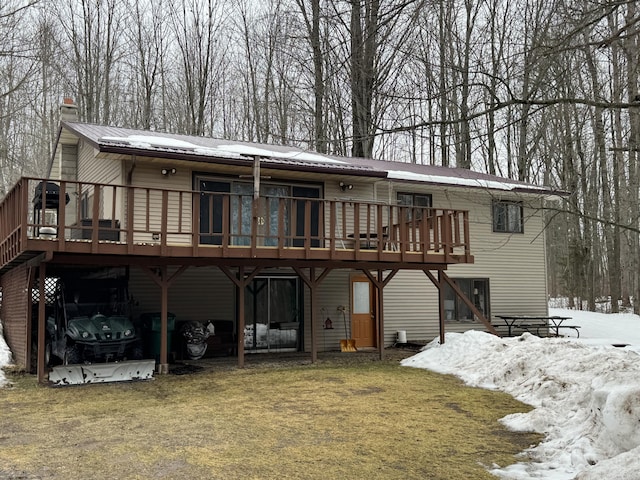 snow covered house with metal roof, a chimney, a wooden deck, and a lawn