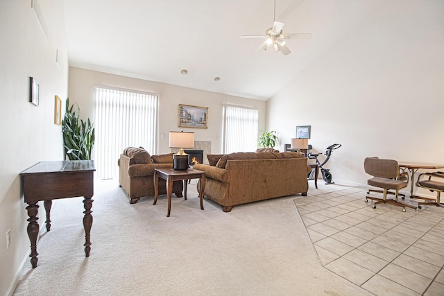 living area with light carpet, baseboards, ceiling fan, a lit fireplace, and high vaulted ceiling