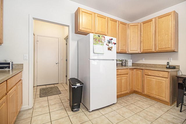 kitchen with freestanding refrigerator, light tile patterned floors, and light brown cabinetry