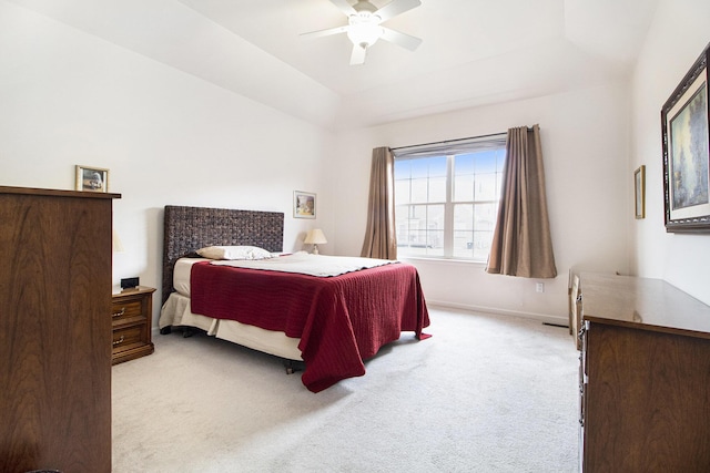 bedroom featuring a raised ceiling, light carpet, ceiling fan, and baseboards