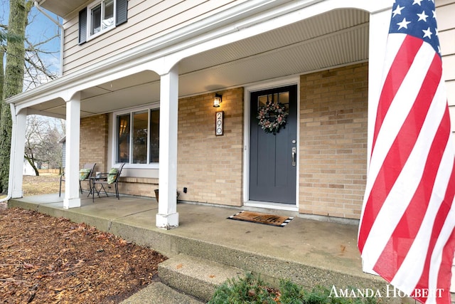 entrance to property with a porch and brick siding