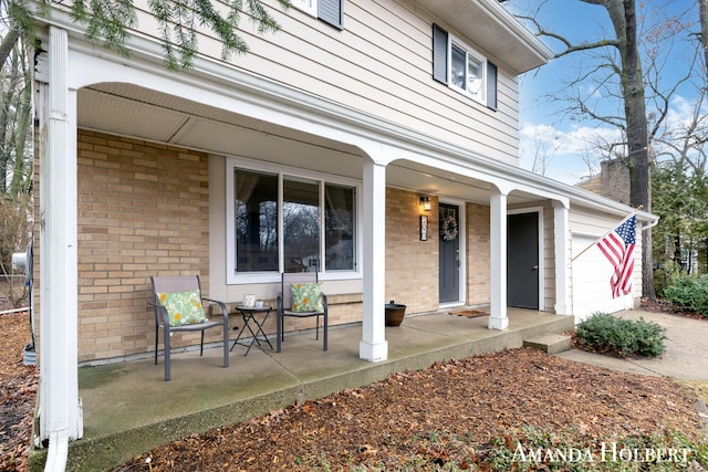 entrance to property featuring covered porch, brick siding, and an attached garage