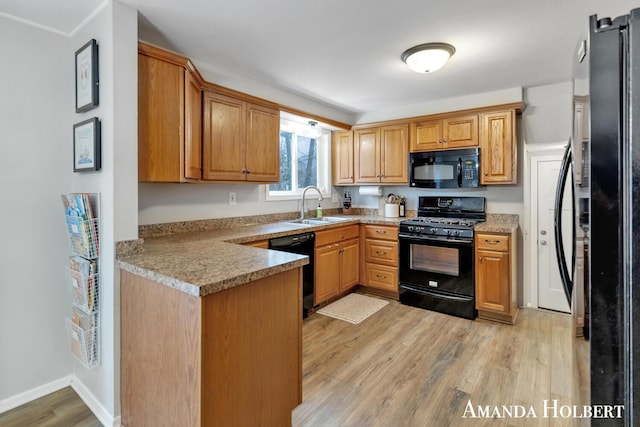 kitchen featuring a peninsula, light countertops, light wood-type flooring, black appliances, and a sink