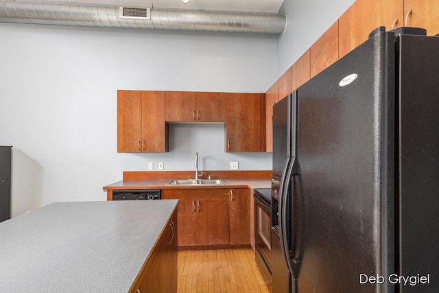 kitchen featuring brown cabinets, visible vents, a sink, light wood-type flooring, and black appliances