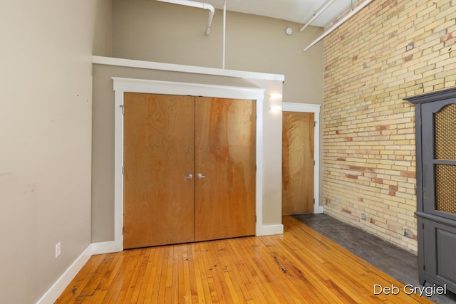 unfurnished bedroom with brick wall, wood-type flooring, baseboards, and a closet