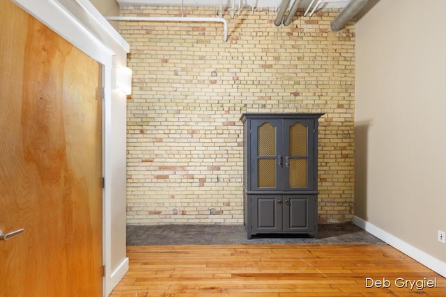 spare room with brick wall, wood finished floors, and baseboards