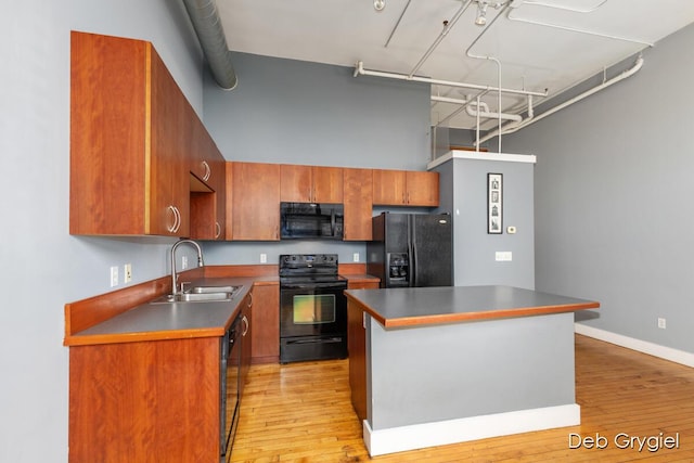 kitchen with dark countertops, light wood-style flooring, a center island, black appliances, and a sink