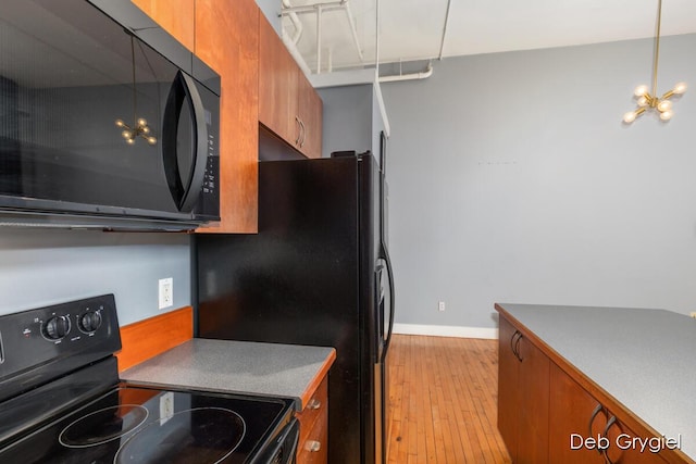 kitchen with brown cabinets, light wood-style flooring, black appliances, modern cabinets, and baseboards