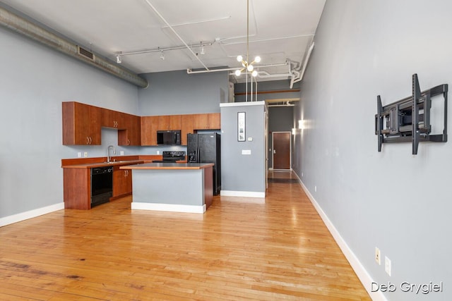 kitchen featuring light wood finished floors, a towering ceiling, rail lighting, black appliances, and a sink