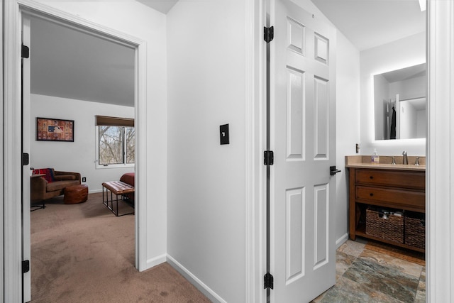 hall featuring a sink, baseboards, and carpet flooring