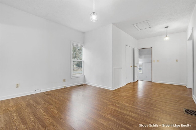 empty room featuring a textured ceiling, wood finished floors, visible vents, and baseboards