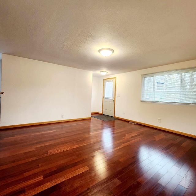 unfurnished room with a textured ceiling, baseboards, and dark wood-style flooring