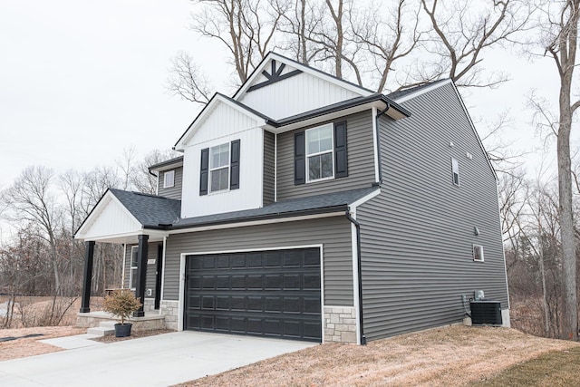 view of front facade featuring an attached garage, central air condition unit, driveway, stone siding, and roof with shingles