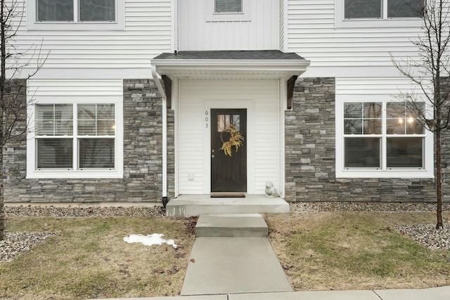 view of exterior entry featuring stone siding and roof with shingles