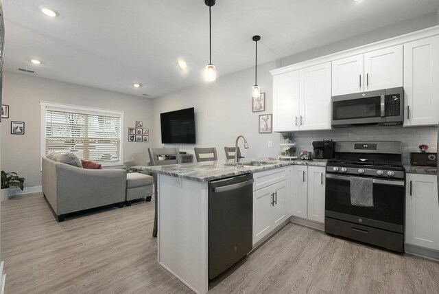 kitchen with decorative backsplash, appliances with stainless steel finishes, open floor plan, a peninsula, and a sink