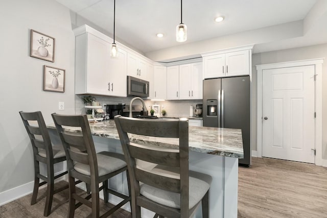 kitchen featuring a peninsula, stainless steel appliances, light wood-type flooring, white cabinetry, and backsplash