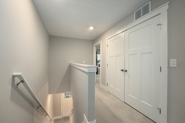 hallway featuring an upstairs landing, visible vents, and light colored carpet