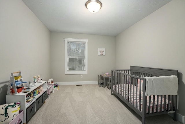 bedroom featuring a crib, baseboards, and light colored carpet