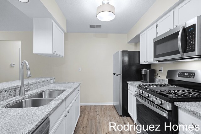 kitchen with stainless steel appliances, light wood-type flooring, white cabinetry, and a sink