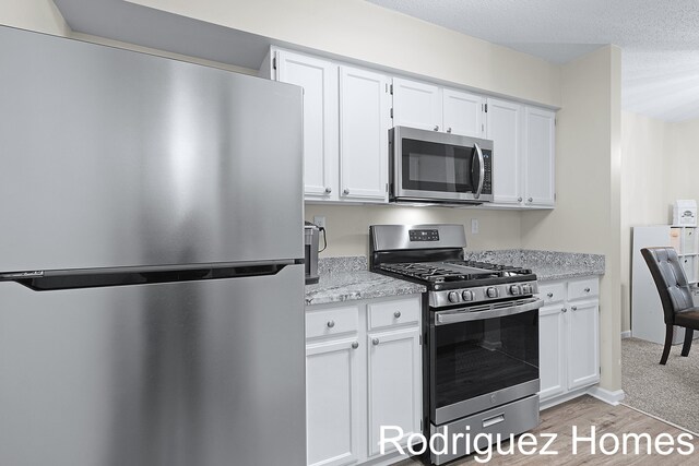 kitchen with appliances with stainless steel finishes, white cabinetry, and light stone countertops