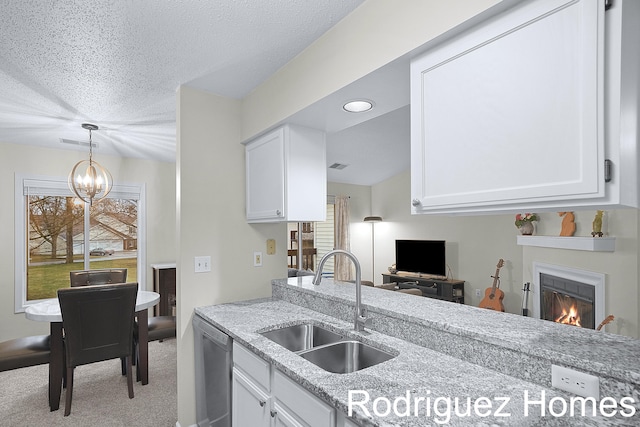 kitchen with visible vents, white cabinets, a sink, a lit fireplace, and stainless steel dishwasher