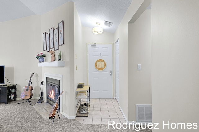 carpeted foyer with baseboards, a fireplace with flush hearth, visible vents, and tile patterned floors