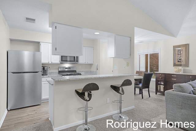 kitchen with visible vents, lofted ceiling, appliances with stainless steel finishes, a breakfast bar area, and white cabinetry