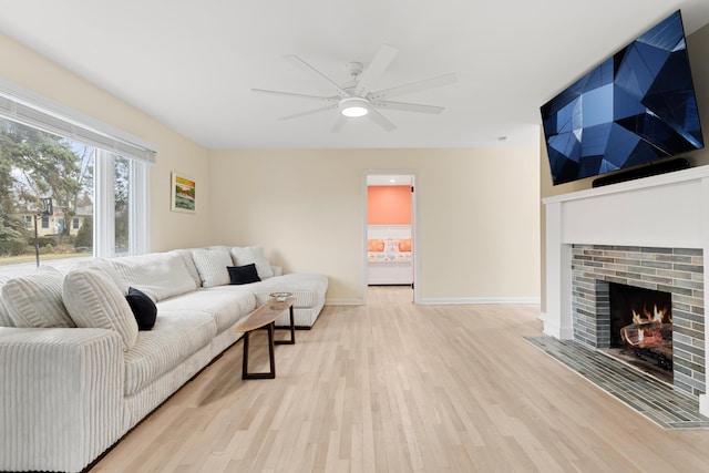 living area featuring light wood-type flooring, a fireplace, baseboards, and a ceiling fan