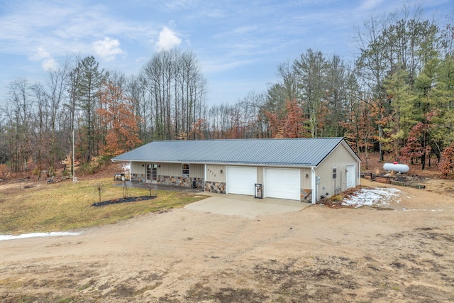 view of front of home featuring stone siding, metal roof, dirt driveway, and an attached garage