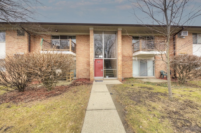 view of exterior entry with a balcony, a wall unit AC, and brick siding