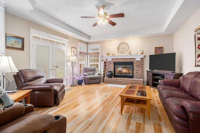 living area featuring light wood-style flooring, a fireplace, a tray ceiling, and french doors