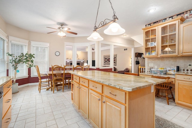 kitchen featuring a center island, tasteful backsplash, light brown cabinetry, glass insert cabinets, and ceiling fan