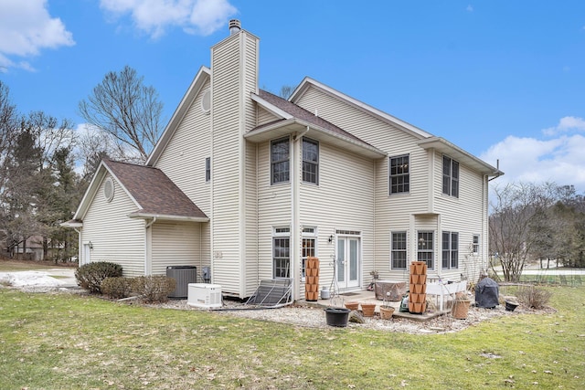 rear view of house featuring roof with shingles, a yard, a chimney, central air condition unit, and a patio area