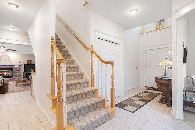 foyer with stairs, a fireplace, a ceiling fan, and baseboards