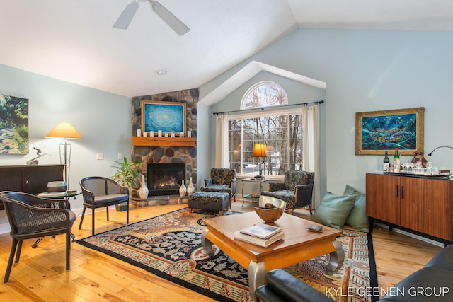 living area featuring ceiling fan, vaulted ceiling, wood finished floors, and a stone fireplace