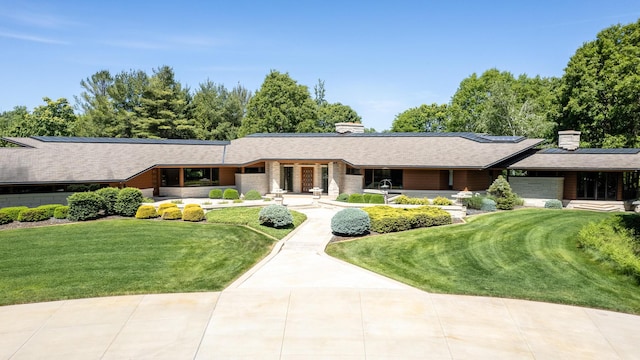 view of front of house with a chimney, solar panels, covered porch, an attached garage, and a front lawn