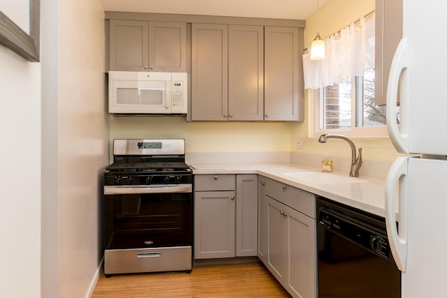 kitchen featuring gray cabinetry, white appliances, a sink, light wood-style floors, and light countertops