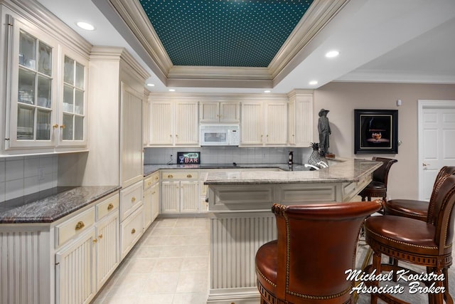 6862 Maplecrest Dr SE, Grand Rapids, MI 49546 - kitchen with white microwave, a raised ceiling, a kitchen bar, a peninsula, and decorative backsplash