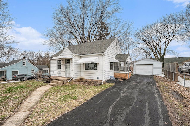 bungalow-style house featuring an outbuilding, a detached garage, fence, driveway, and roof with shingles