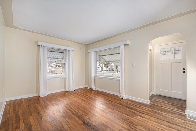 spare room featuring wood-type flooring, arched walkways, and baseboards