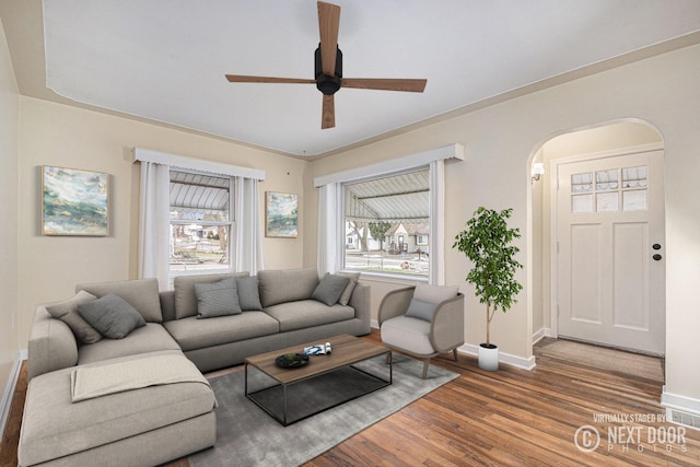 living area with arched walkways, ceiling fan, baseboards, and wood finished floors