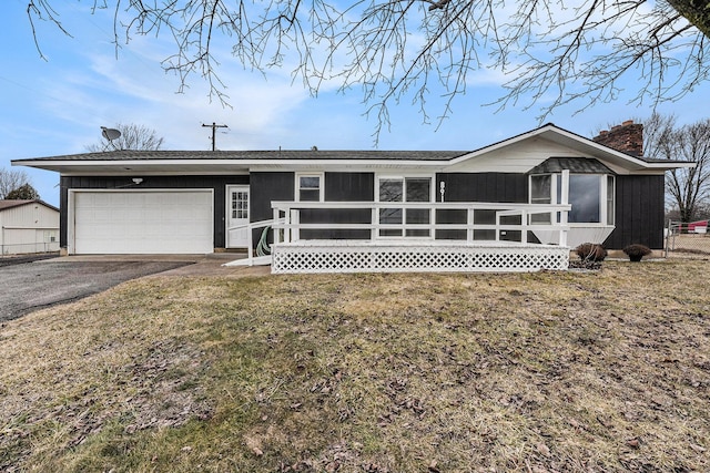 ranch-style home with a garage, a chimney, a front lawn, and aphalt driveway