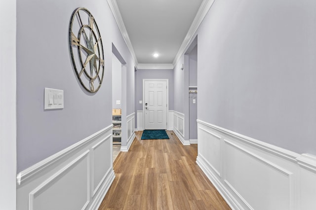 hallway featuring a wainscoted wall, crown molding, light wood-style flooring, and a decorative wall