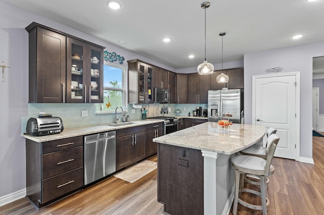 kitchen featuring a kitchen island, appliances with stainless steel finishes, a sink, dark brown cabinets, and backsplash