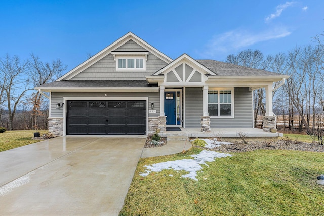 craftsman-style home featuring driveway, a shingled roof, stone siding, covered porch, and a front yard