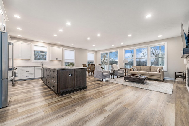 kitchen featuring white cabinets, open floor plan, a center island, light countertops, and light wood-style floors