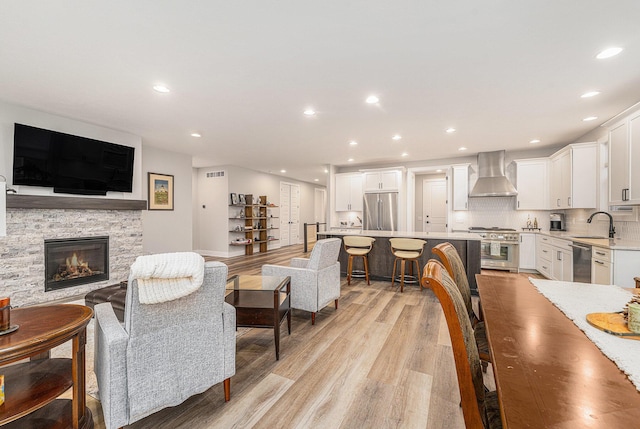 living room with visible vents, a stone fireplace, light wood-style flooring, and recessed lighting