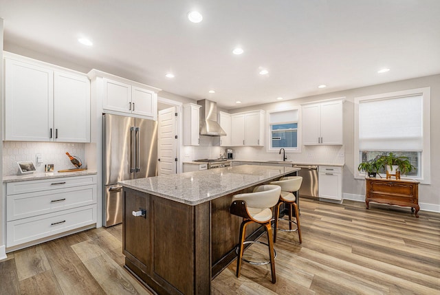 kitchen with appliances with stainless steel finishes, a center island, light wood-type flooring, and wall chimney range hood