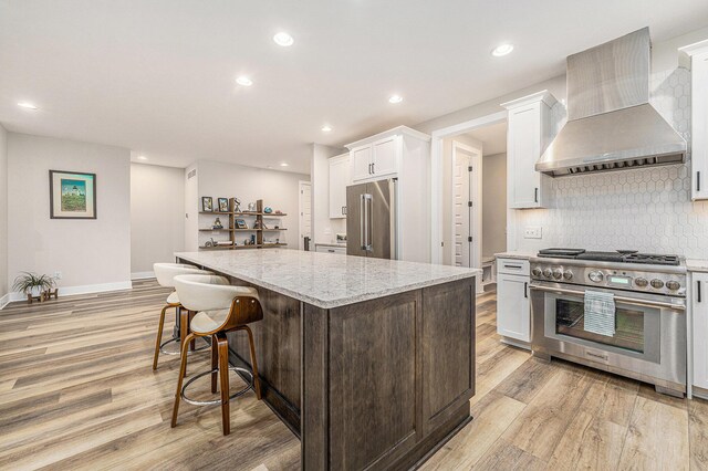 kitchen with light wood-style flooring, a kitchen island, wall chimney range hood, and high quality appliances